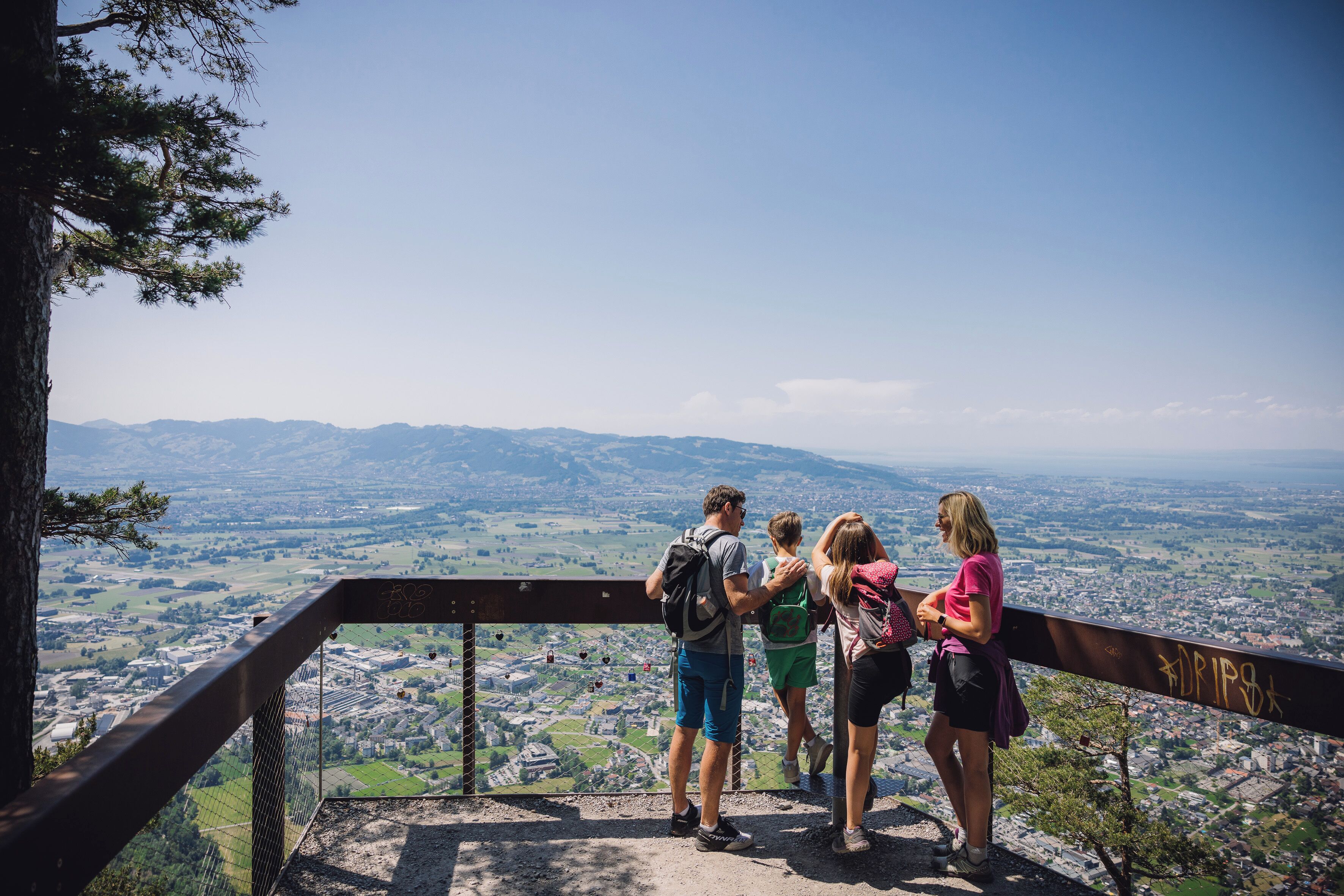 A group of people standing on a viewing platform with a panoramic view of a city and mountains.