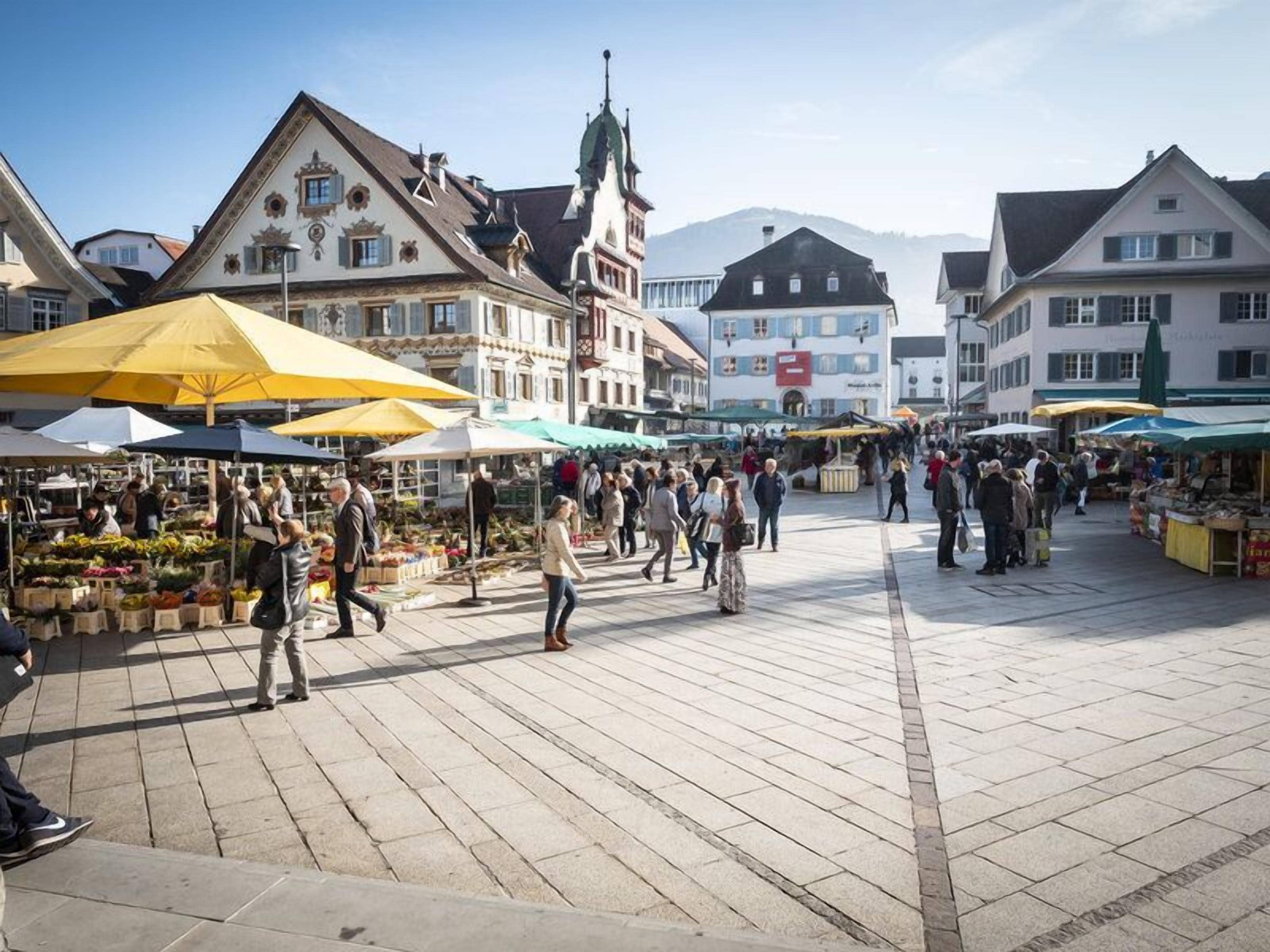 A bustling outdoor market with vendors and shoppers, surrounded by historic buildings with traditional architecture.