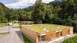 A modern building with a flat roof covered in grass, surrounded by a forested area.