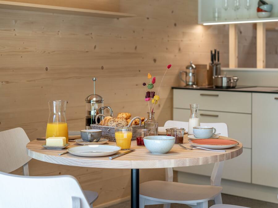 A breakfast table set with various breakfast items, including a bottle of orange juice, a glass of milk, and a basket of pastries.
