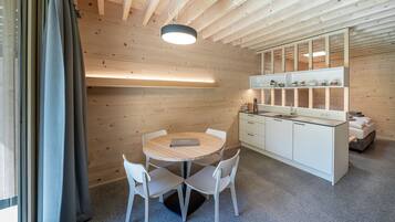 A modern kitchen with a round wooden table and white chairs, a white countertop, and a built-in shelf with kitchen items.