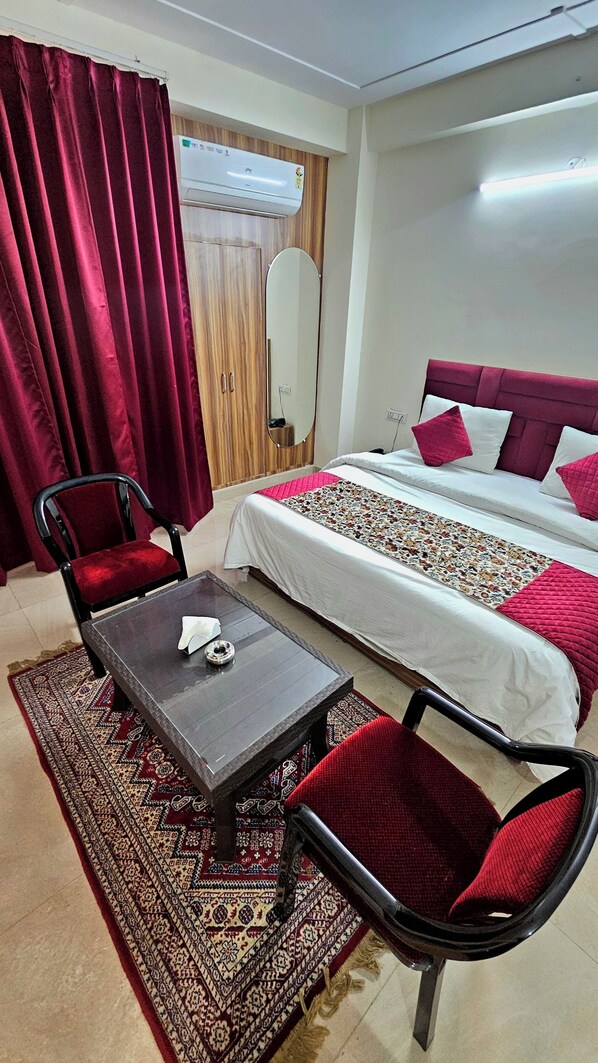 A hotel room with a bed, a desk, two chairs, a mirror, and a red curtain.