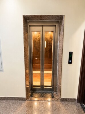 An elevator with a digital display, a marble floor, and a textured wall. - Hotel Trident Dwarka (New Delhi)