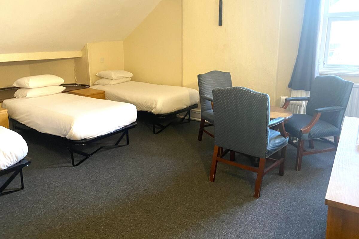 A small, compact room with two single beds, a wooden table, two chairs, and a radiator.