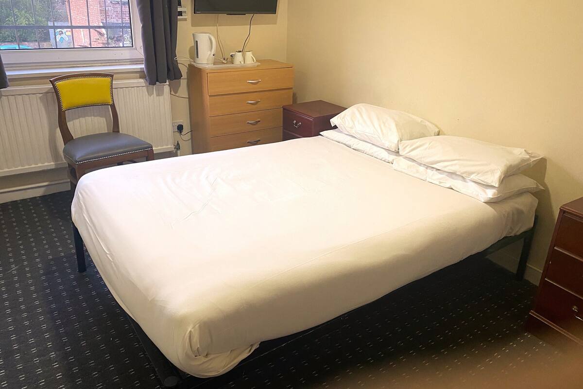 A hotel room with a bed, a chair, a dresser, a television, and a window with curtains.