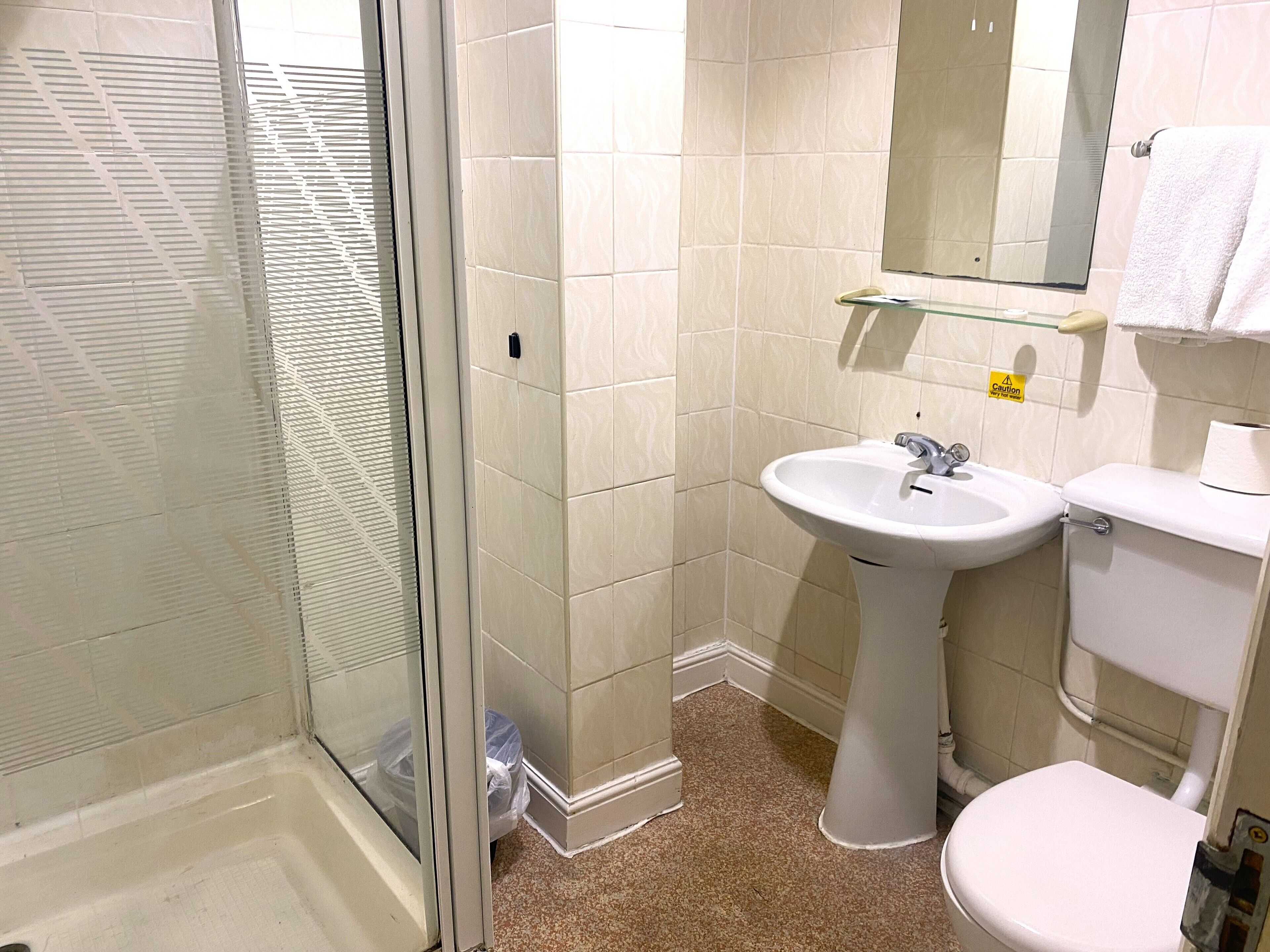 Une salle de bain avec une douche à parois de verre, un lavabo sur colonne et des toilettes.