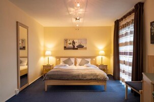 A hotel room with a large bed, two bedside tables with lamps, a mirror, a painting on the wall, and a window with curtains.