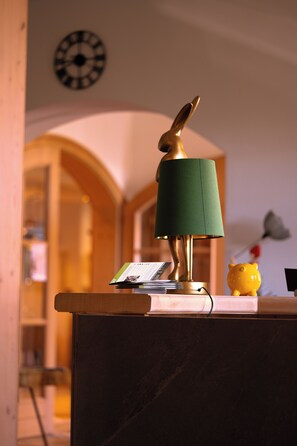 Una lampada con un paralume verde e una base dorata, una piccola statuina gialla e un orologio appeso al muro.