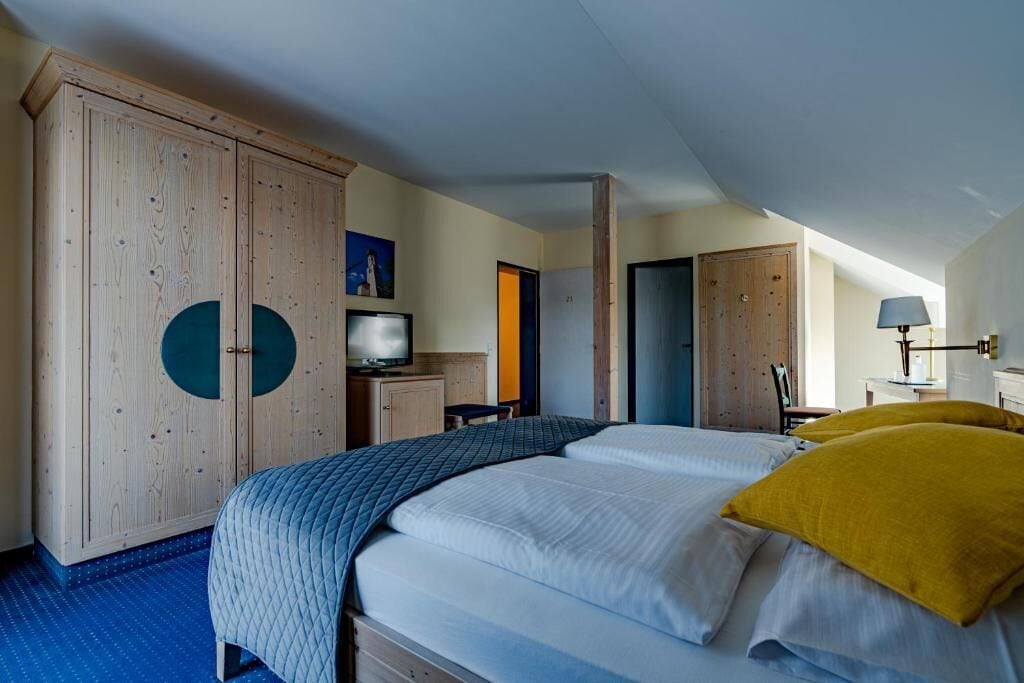 A hotel room with a large bed, a wardrobe, a desk with a computer, and a lamp.