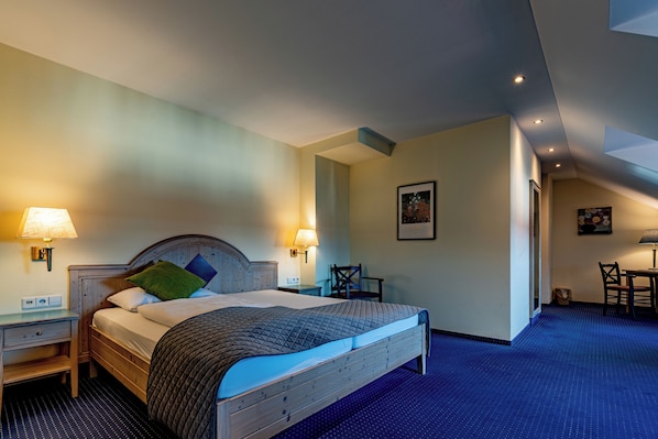 Quarto de hotel com uma cama grande, duas mesas de cabeceira com luminárias, uma escrivaninha e uma cadeira.