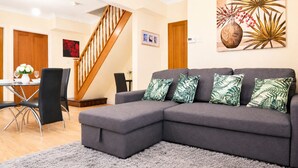 A modern living room with a grey sectional sofa, a dining area with a table and chairs, a staircase, and a wall with a large floral painting. - Stunning 3-Bed House in the Heart of Newport, Sleeps 7 (Newport)