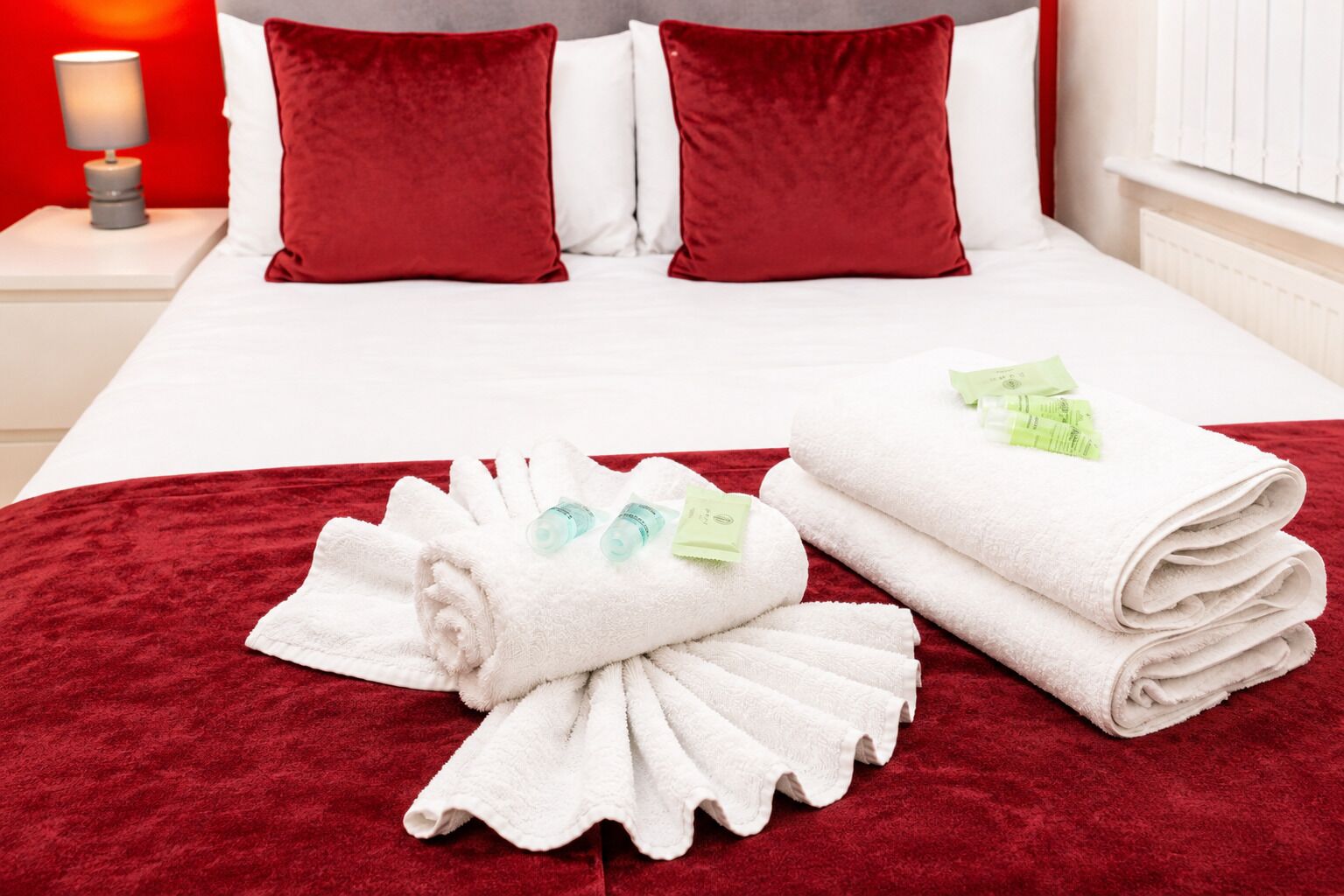 Une chambre d’hôtel avec un lit bien fait, des oreillers rouges, du linge de lit blanc et des serviettes accompagnées de produits de toilette.