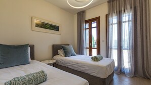 Een hotelkamer met twee bedden, een klein nachtkastje, een lijst aan de muur en een raam met gordijnen.