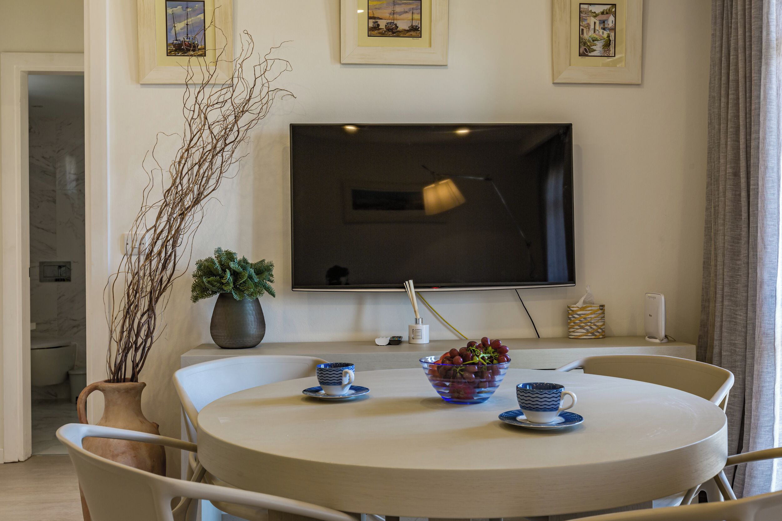Un comedor con una mesa redonda, sillas, un televisor montado en la pared y fotografías enmarcadas sobre el televisor.