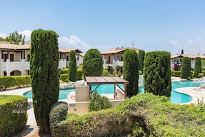 A pool area with a gazebo, neatly trimmed hedges, and a building with balconies. - Db11 Adjacent to Aphrodite Hills Communal Pool Retreat (Kouklia)