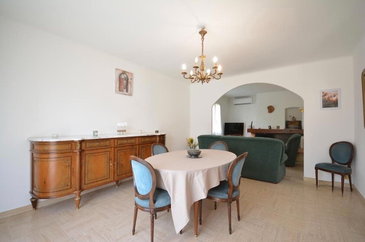 A dining area with a round table, chairs, a chandelier, and a wooden cabinet.