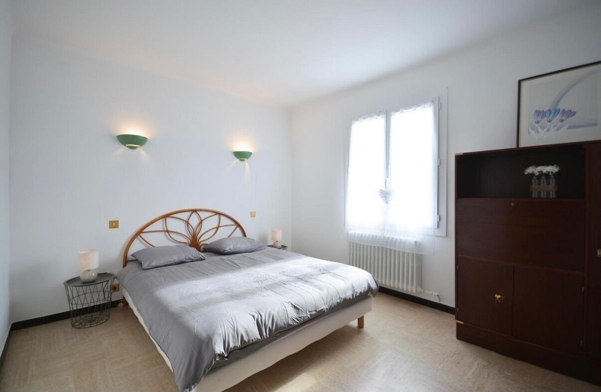 Une chambre à coucher comprenant un lit, deux lampes fixées au mur, un radiateur, une fenêtre et une armoire.