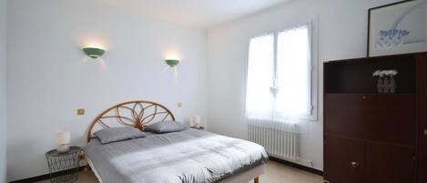 Une chambre à coucher comprenant un lit, deux lampes fixées au mur, un radiateur, une fenêtre et une armoire.