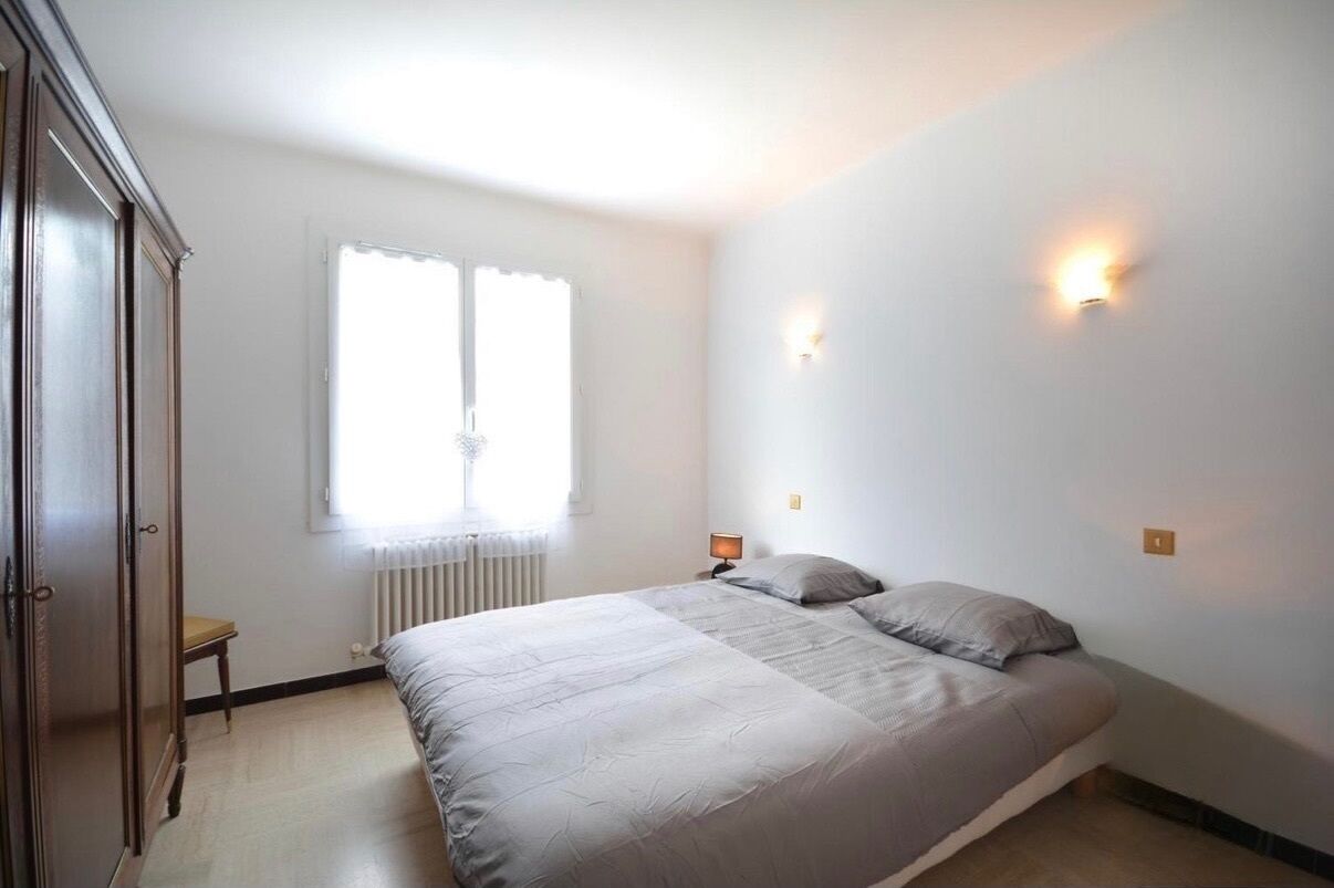 Een slaapkamer met een bed, een radiator, een raam met gordijnen en een kledingkast.