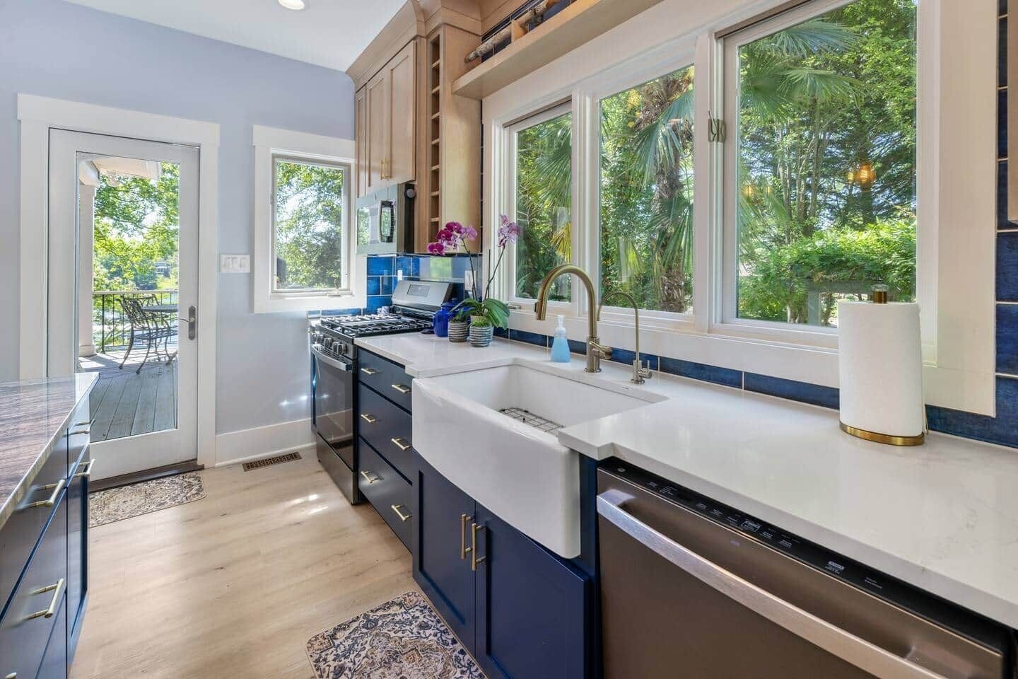 A modern kitchen with a large island, built-in appliances, and large windows offering a view of greenery.
