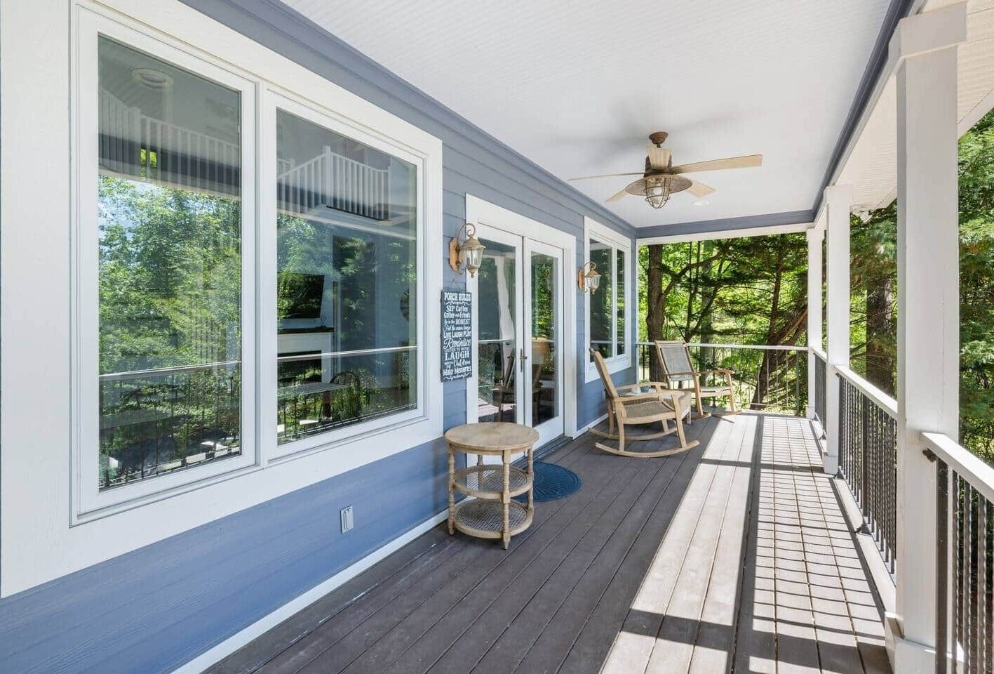 A covered porch with a ceiling fan, large windows, and wooden rocking chairs.