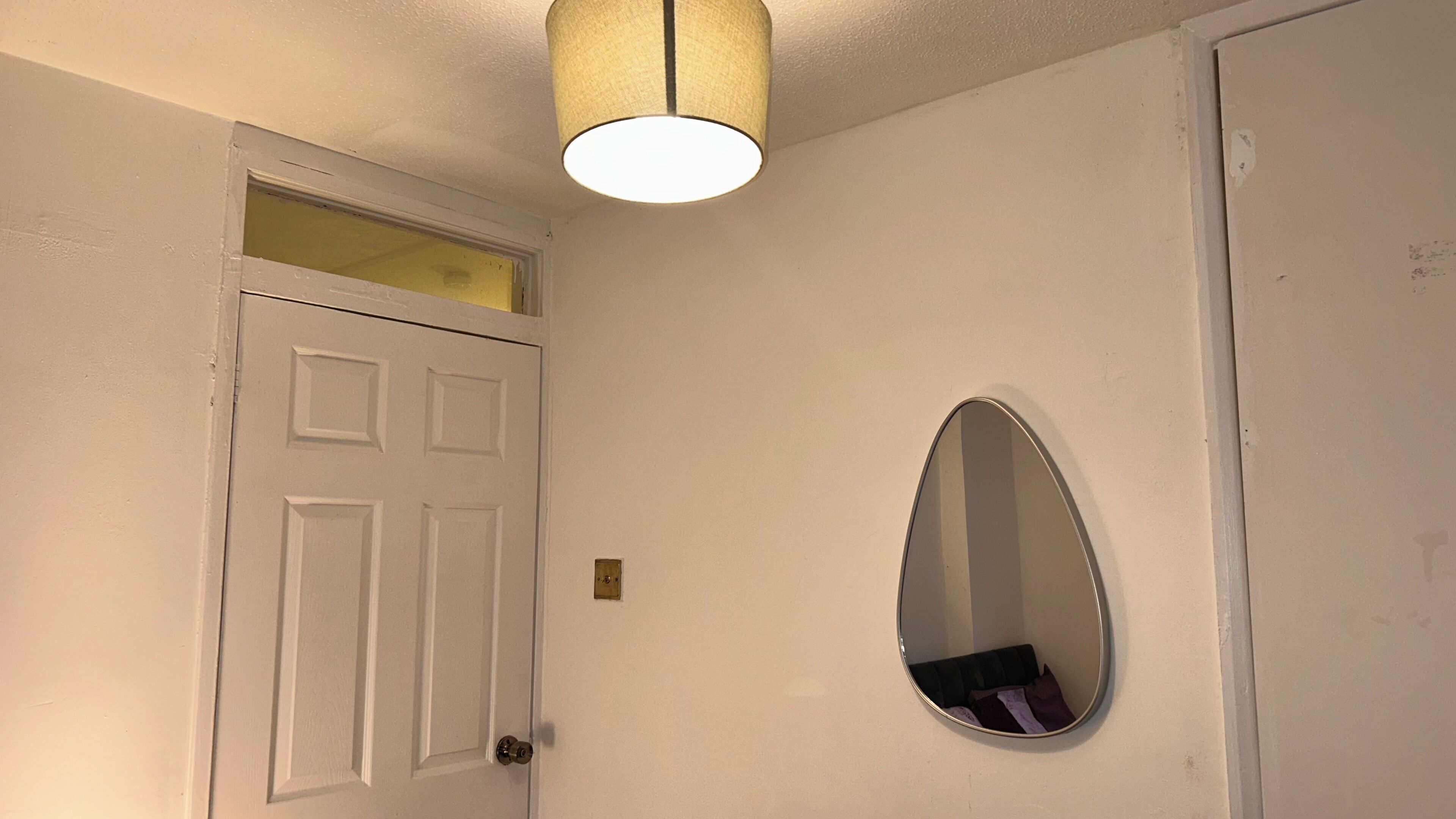 A white door with a small window above it, a round mirror on the wall, and a ceiling light fixture.