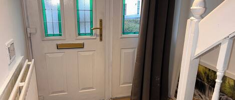 A white door with green-tinted windows, a brass door handle, and a black mat at the entrance.