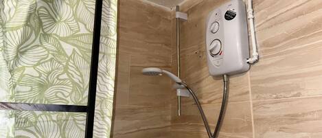 A shower with a handheld showerhead and a control panel, a tiled wall, and a patterned curtain.