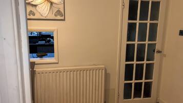 Een kamer met een witte radiator, een witte deur met glaspanelen en een raam met uitzicht op een keuken.