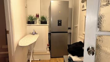 A compact kitchen with a refrigerator, an ironing board, and a water dispenser.