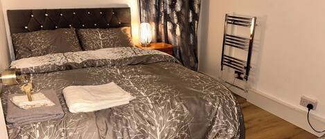 A neatly made bed with a patterned duvet, a bedside lamp, and a wall-mounted towel rack.
