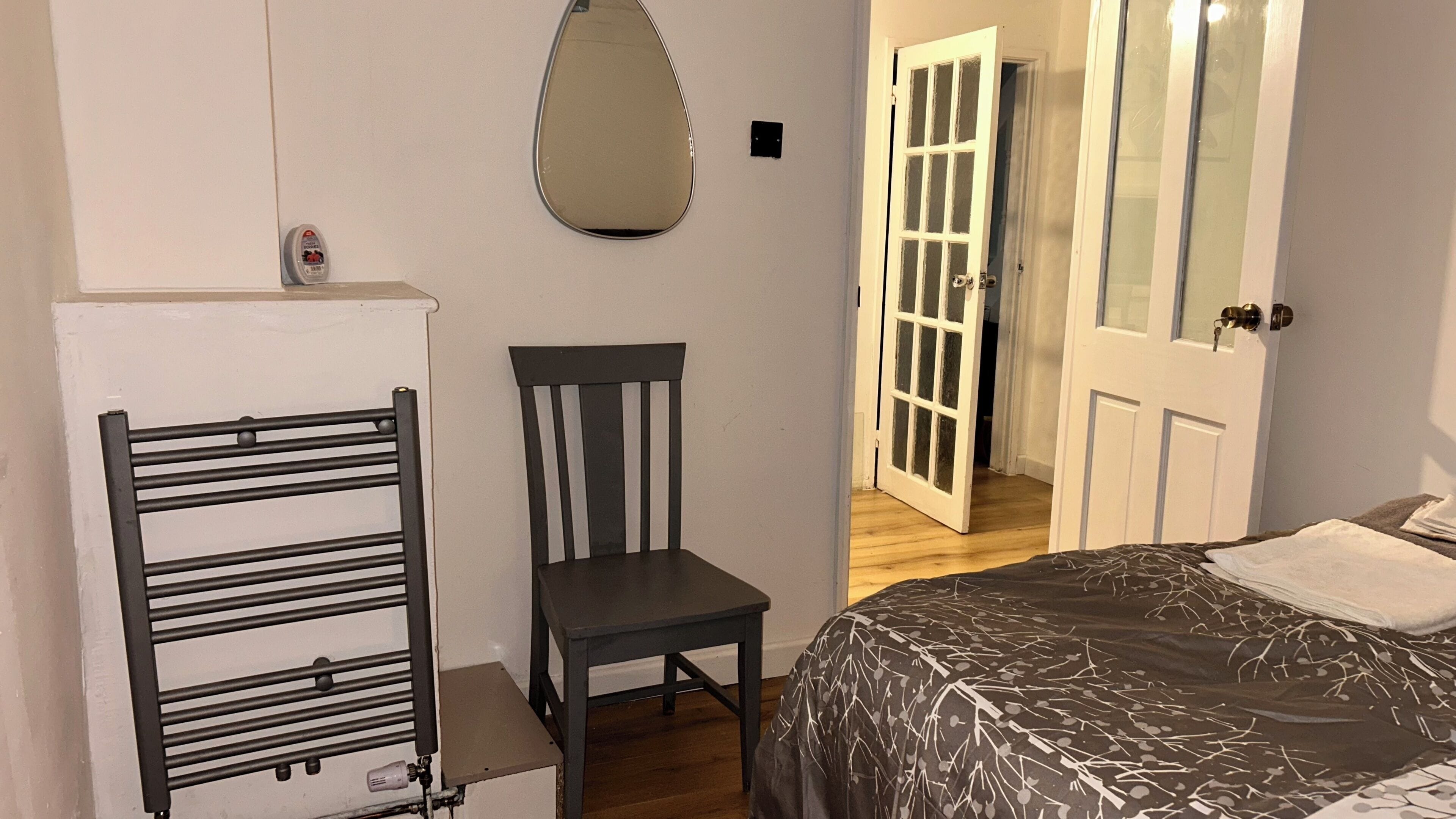 Un dormitorio con una cama, una silla, un radiador y una puerta que da a otra habitación.
