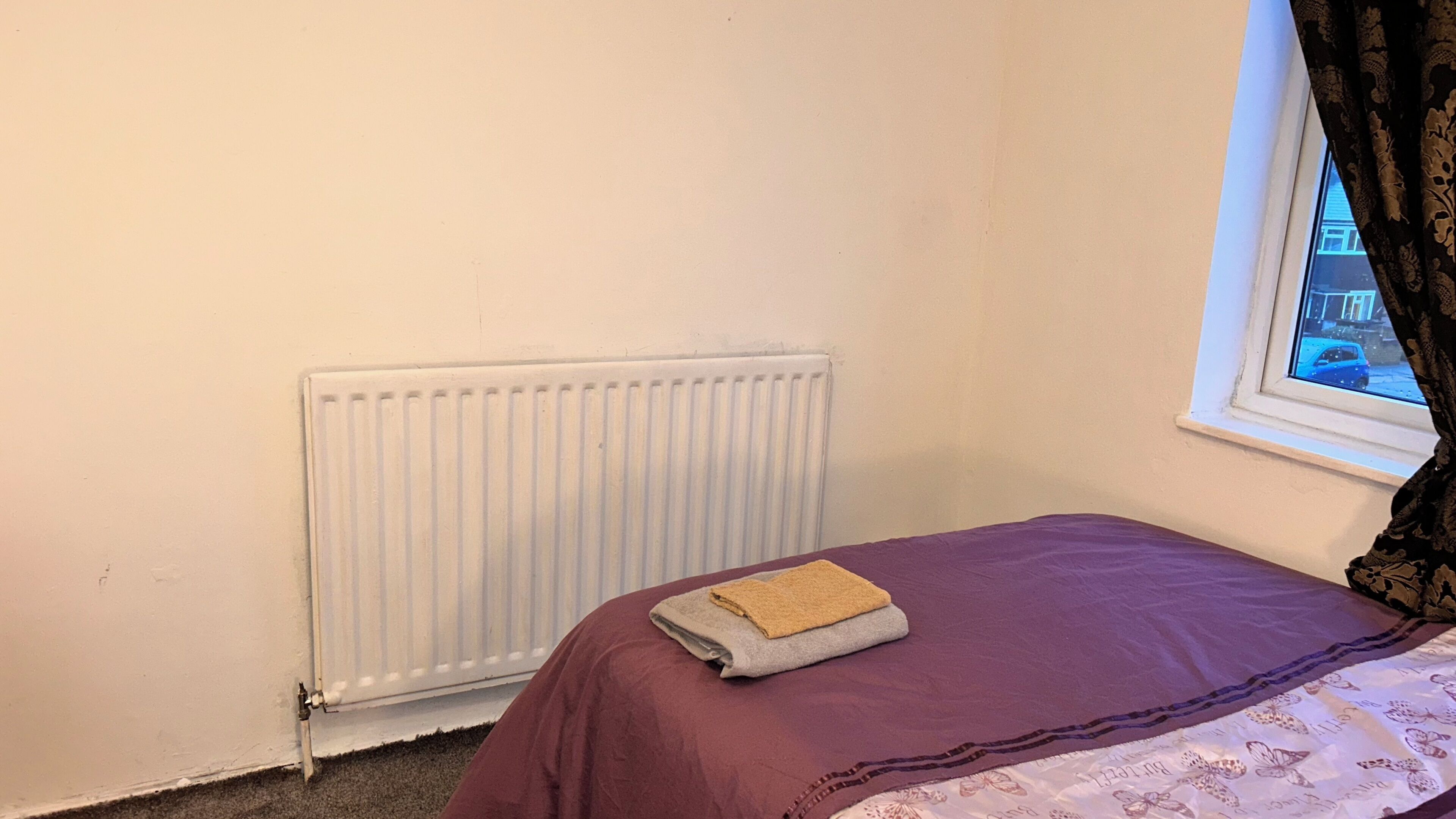 A small room with a single bed, a radiator, and a window with curtains.
