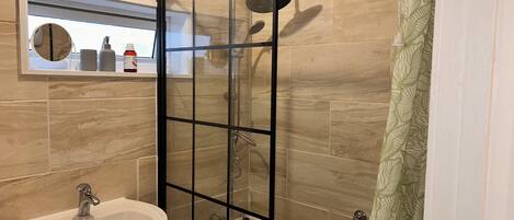 A bathroom with a glass shower enclosure, a sink, and a mirror above it.