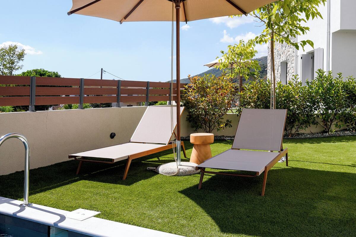 Un área junto a la piscina con piscina, dos sillones de descanso y una sombrilla grande.