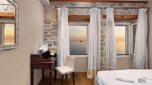 A bedroom with a stone wall, a wooden ceiling, a desk with a chair, a bed, and a view of the sea through large windows with white curtains. - Dimore Apartment Monte (Rovinj)