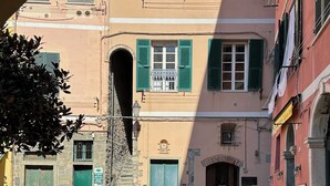 Eine schmale Gasse mit Häusern, die grüne Fensterläden und ein steinernes Tor haben.