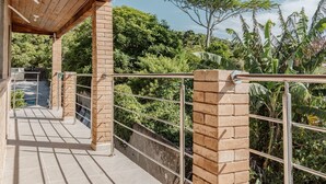 A covered outdoor area with a brick wall and metal railing, overlooking a lush garden. - Apto Perto da Praia Com Piscina e Churrasqueira (Penha)