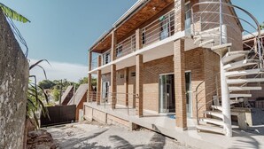 A modern two-story building with a brick facade, a covered outdoor area, and a spiral staircase. - Apto Perto da Praia Com Piscina e Churrasqueira (Penha)