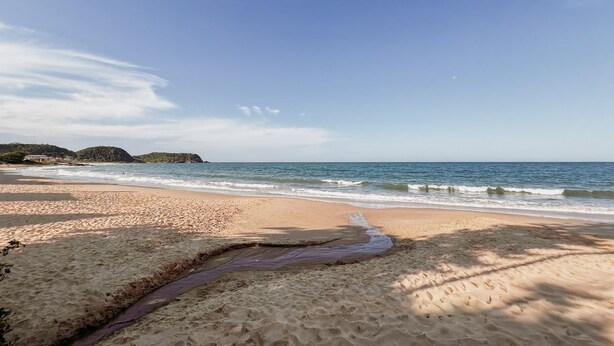 A beach with clear skies, calm waves, and distant hills. - Apto Perto da Praia Com Piscina e Churrasqueira (Penha)