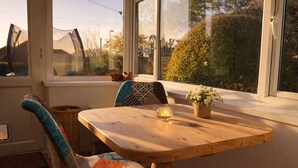 A cozy seating area with a wooden table, a cushioned bench, and a window with a view of trees and a building.