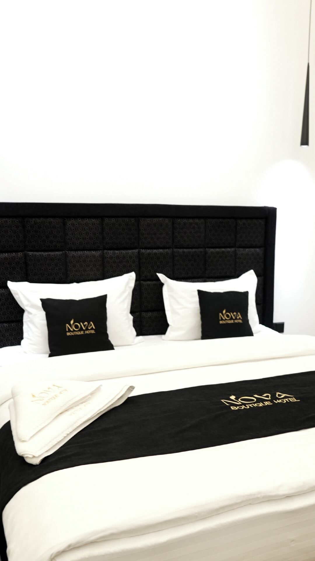 A bed with a black headboard and white bedding, featuring the 'NOVA Boutique Hotel' logo on pillows and a blanket.