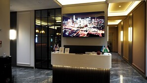 Zona de recepción de hotel con una gran pantalla mostrando un paisaje urbano, una mesa de recepción y banderas.
