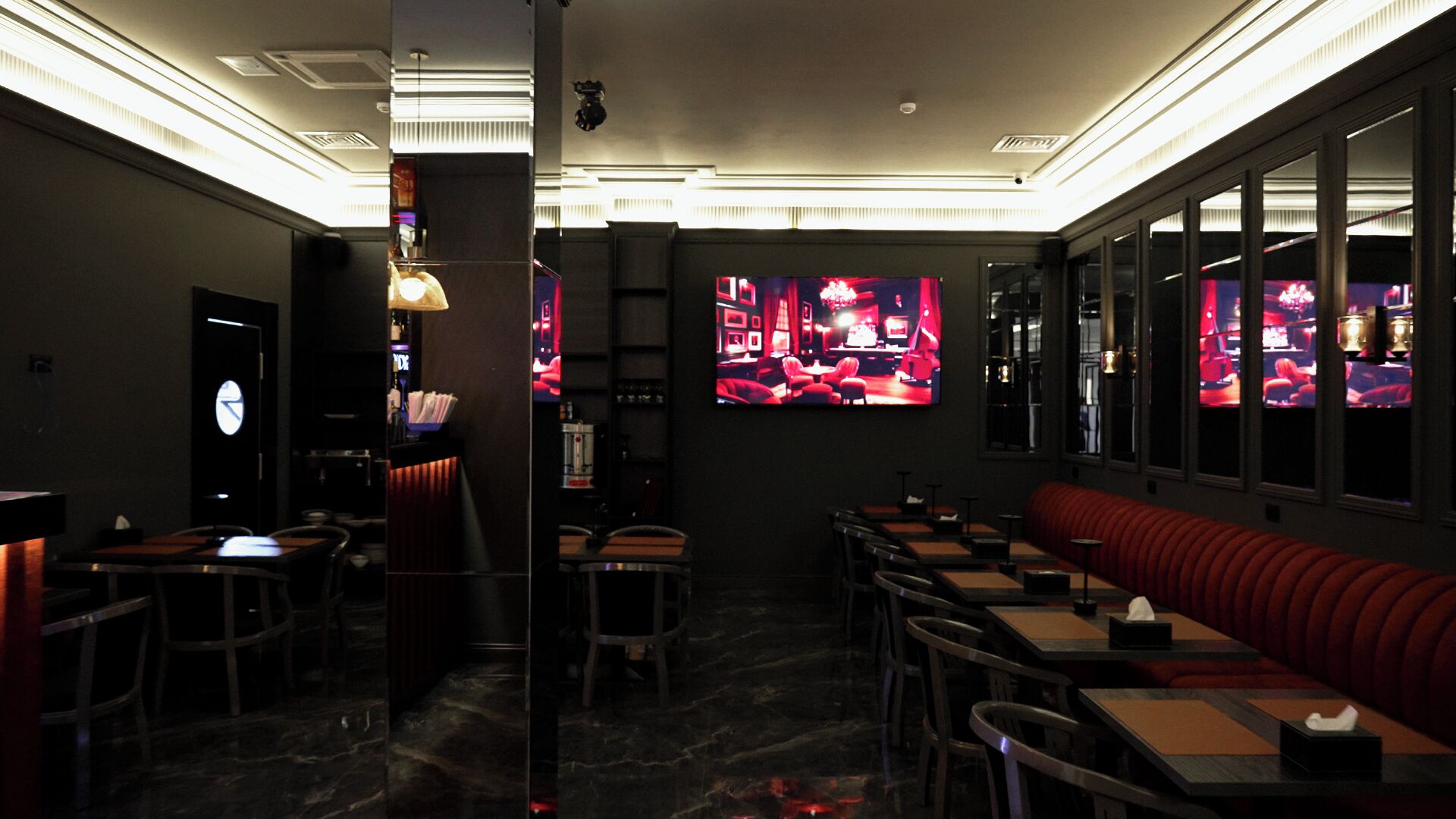 A dimly lit restaurant with tables and a red booth, a clock on the wall, and a TV screen displaying a red-lit interior.
