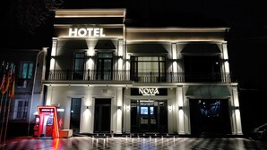 Un hotel con un letrero grande que dice 'HOTEL', un letrero boutique 'NOVA' y un cajero automático visible en la planta baja.