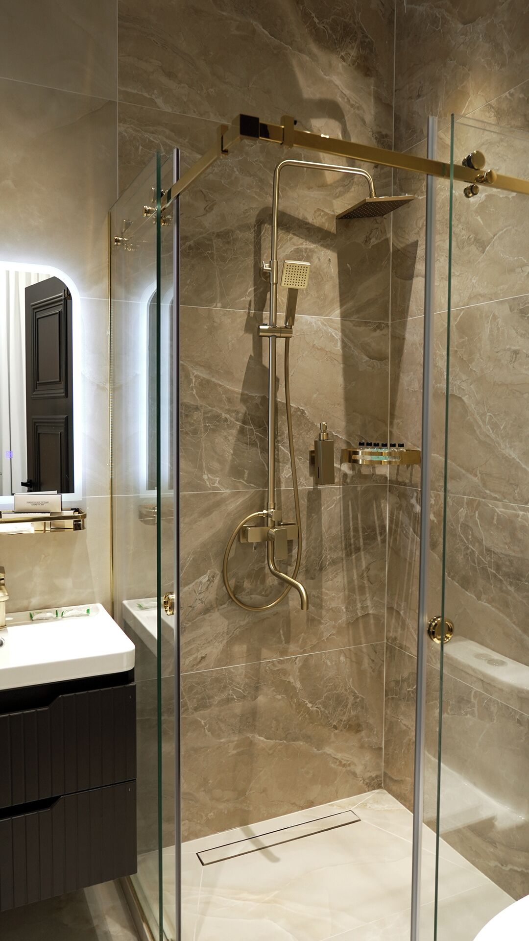 A modern shower enclosure with a glass door, a handheld showerhead, and a wall-mounted control panel.