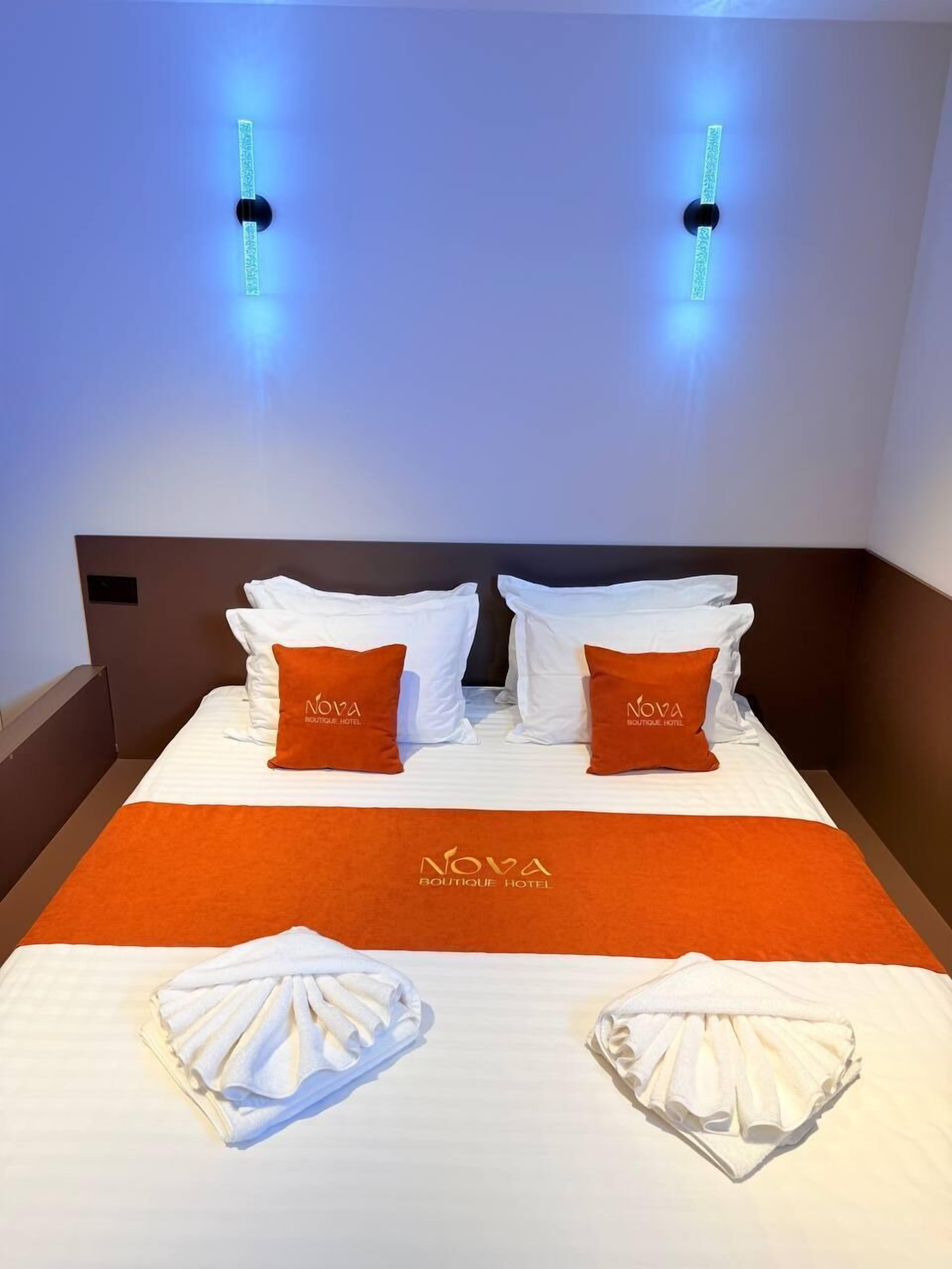 A hotel room with a bed, two pillows with the hotel's logo, a headboard, and two wall-mounted light fixtures.