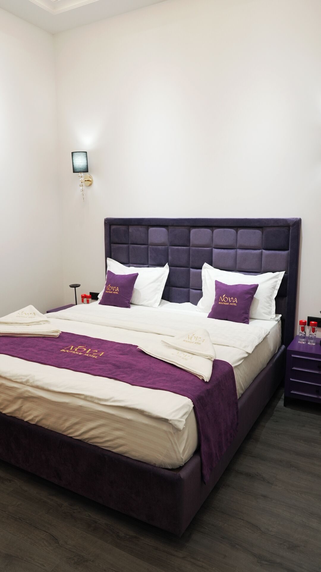 Una habitación de hotel con una cama grande, cabecera, mesita de noche y una lámpara de pared.