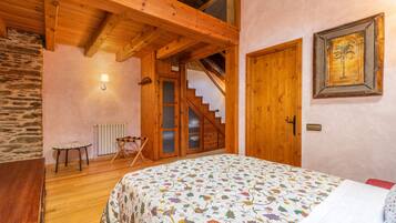 A bedroom with a wooden ceiling, a bed with a floral bedspread, a wooden door, a staircase, and a stone wall.