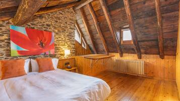 Una habitación con techo inclinado, paredes de madera, una cama con ropa blanca, un cuadro de una flor roja y una ventana.